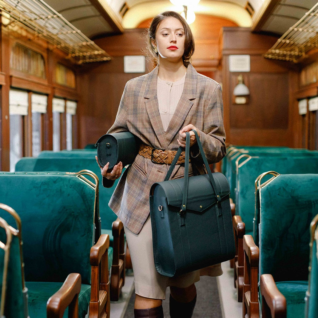 Woman holding two bags in a train carriage with green seats and wooden walls.